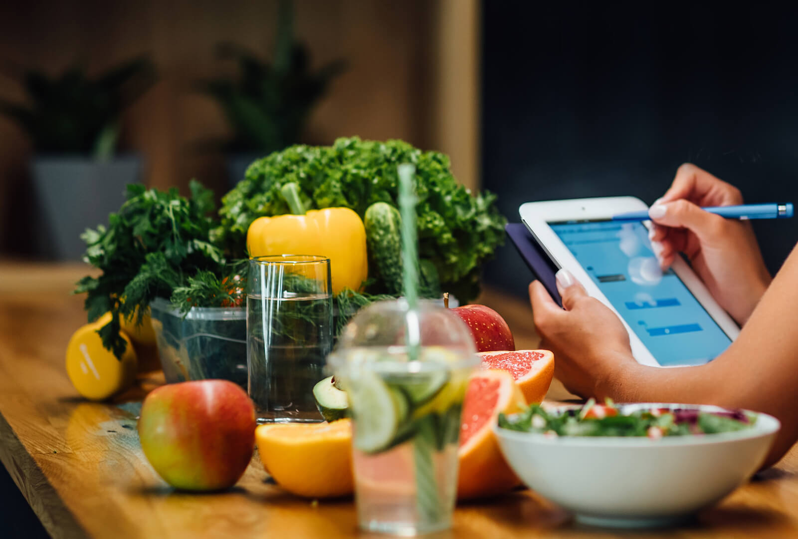 A woman sitting at a counter covered with healthy foods looking at a tablet