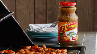 LA VICTORIA<sup>®</sup> Verde Habaneor Salsa next to a grill with marinated shrimp on it.