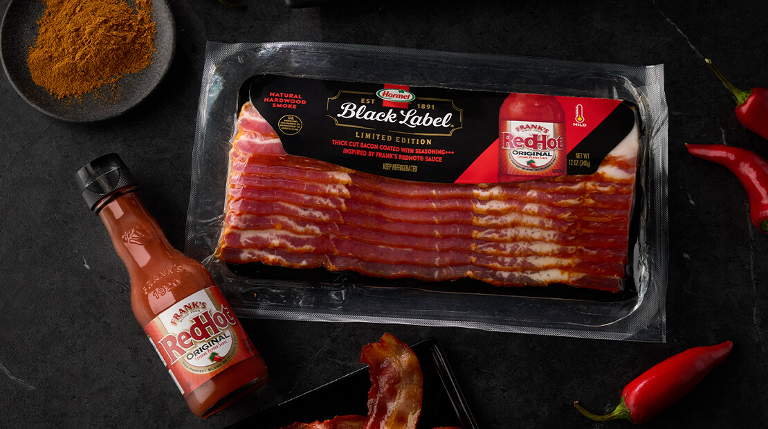 HORMEL® BLACK LABEL® Frank's RedHot® flavored bacon on a black counter top.