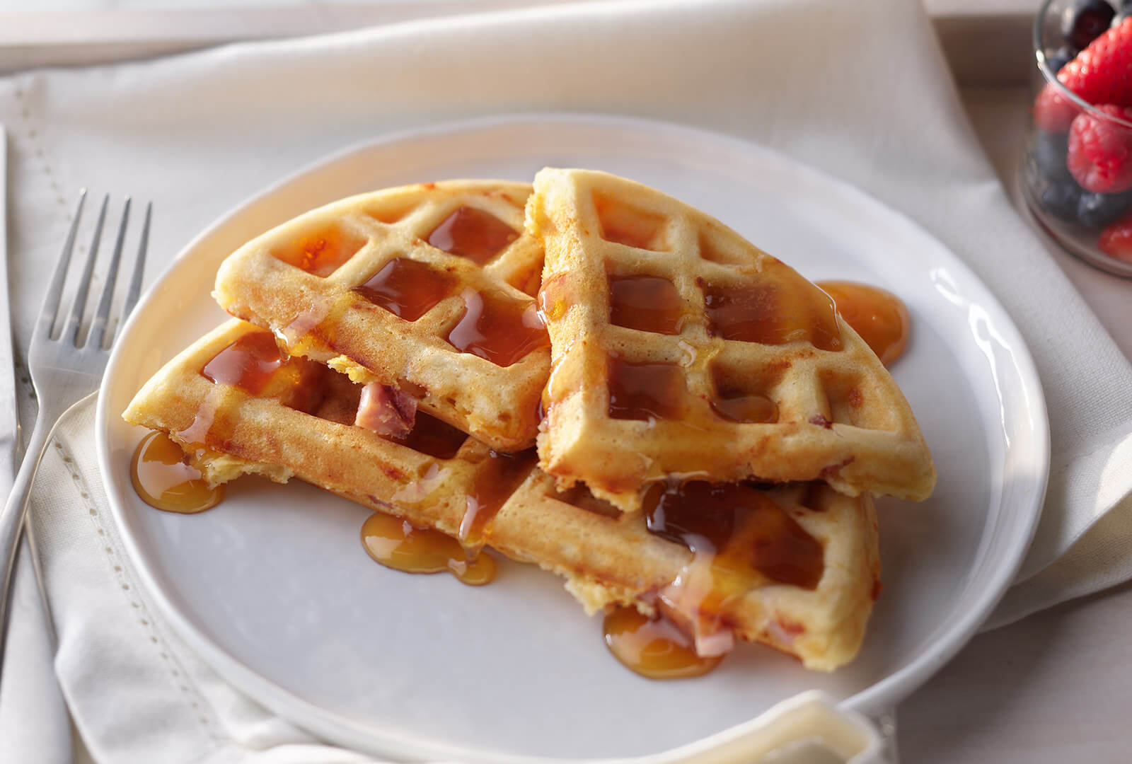 Savory Ham and Cheddar Waffles covered in maple syrup on a white plate