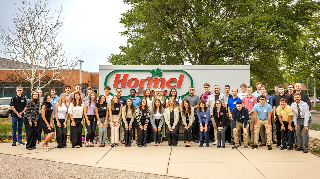 Interns standing in front of the Hormel Foods global headquarters sign.
