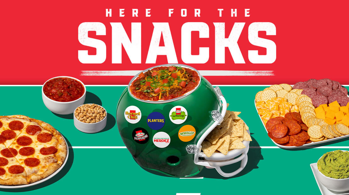 A pepperoni pizza, helmet with salsa on top, a meat and cheese tray and a tub of guacamole on a green football field background.