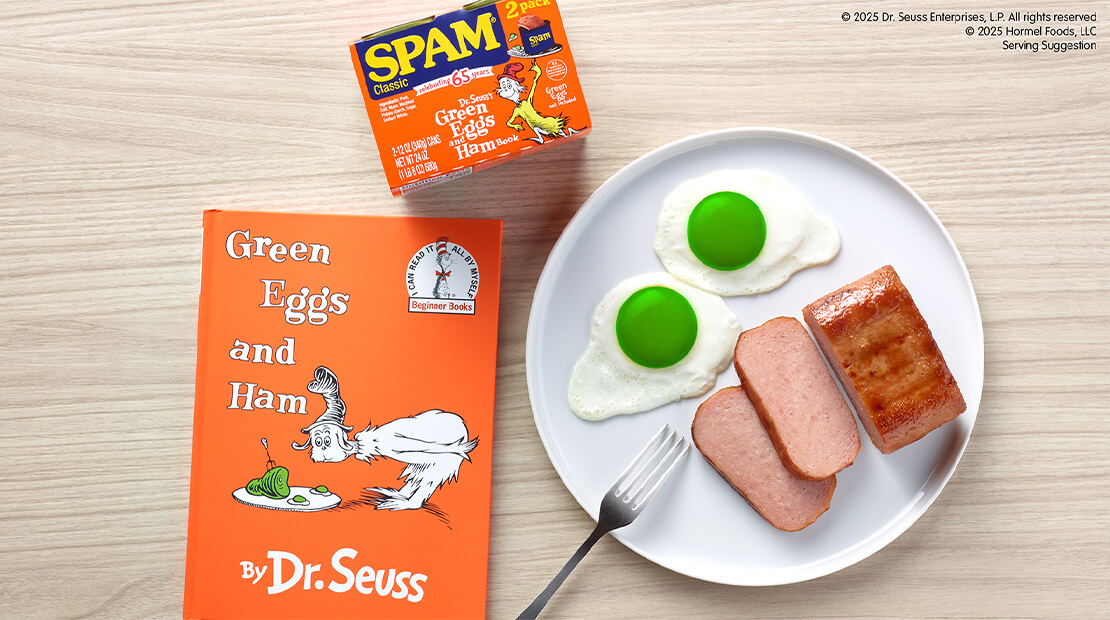 A white plate with eggs with green yolks and fried SPAM® Classic. Next to the plate is the limited-time-only Green Eggs & SPAM Classic Twin Pack. Dr. Seuss’s Green Eggs and Ham is under the twin pack and to the left of the plate.