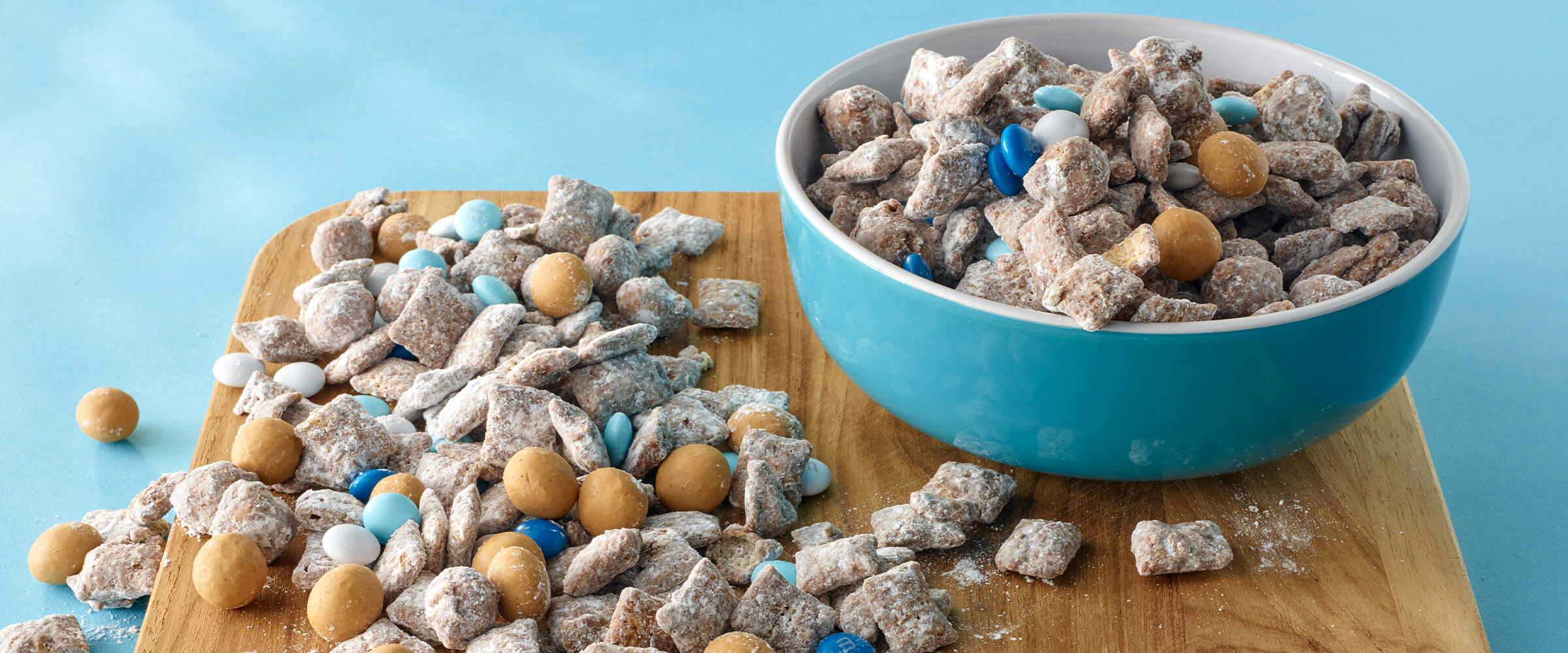 A teal bowl with SKIPPY® P.B. Bites Snowball Munch sitting on a wooden board with more mix on top.