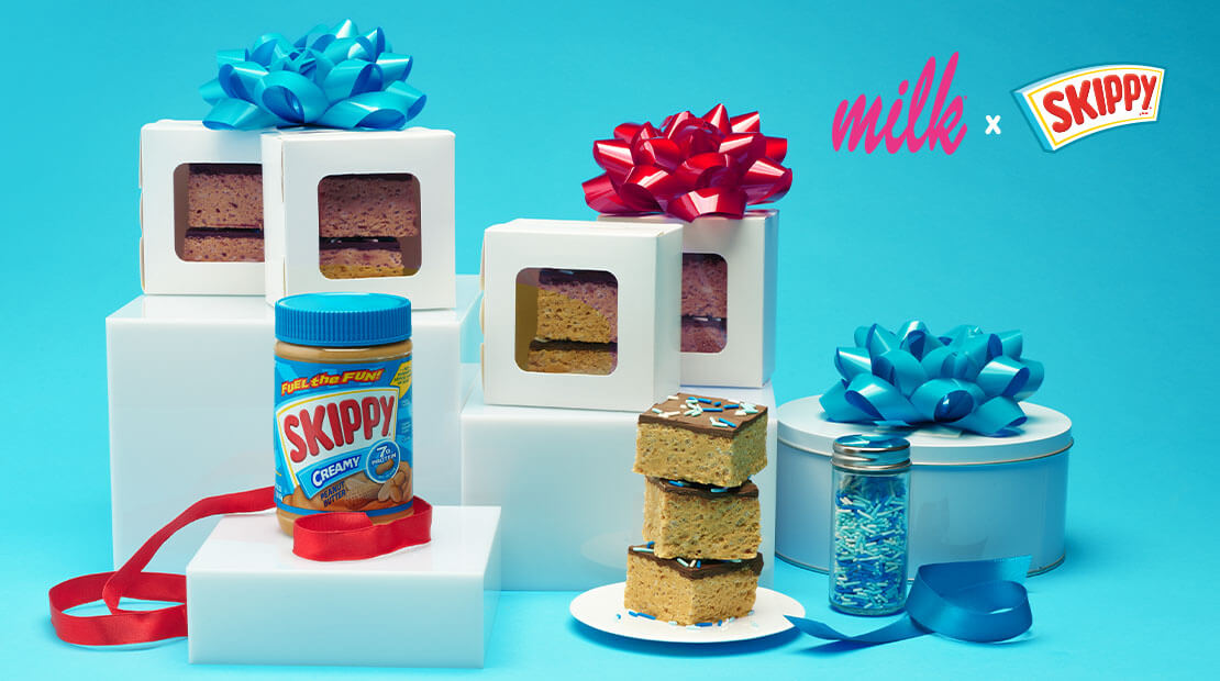 Boxes on white stands and a jar of SKIPPY® Peanut butter on a white stand. Next to the stands is a stack of peanut butter bars and a gift box wrapped with teal ribbon.