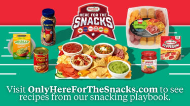 A football‑themed snack display featuring various HORMEL<sup>®</sup> brands arranged around a large platter of chips, dips, nuts, and sliced meats. Surrounding the platter are WHOLLY<sup>®</sup> Guacamole, HORMEL<sup>®</sup> Chili with No Beans, PLANTERS<sup>®</sup> peanuts, a HORMEL GATHERINGS<sup>®</sup> party tray, HERDEZ<sup>®</sup> salsa, and HORMEL<sup>®</sup> pepperoni. At the top is a banner reading ‘Here for the Snacks,’ and at the bottom text reads, ‘Visit OnlyHereForTheSnacks.com to see recipes from our snacking playbook.