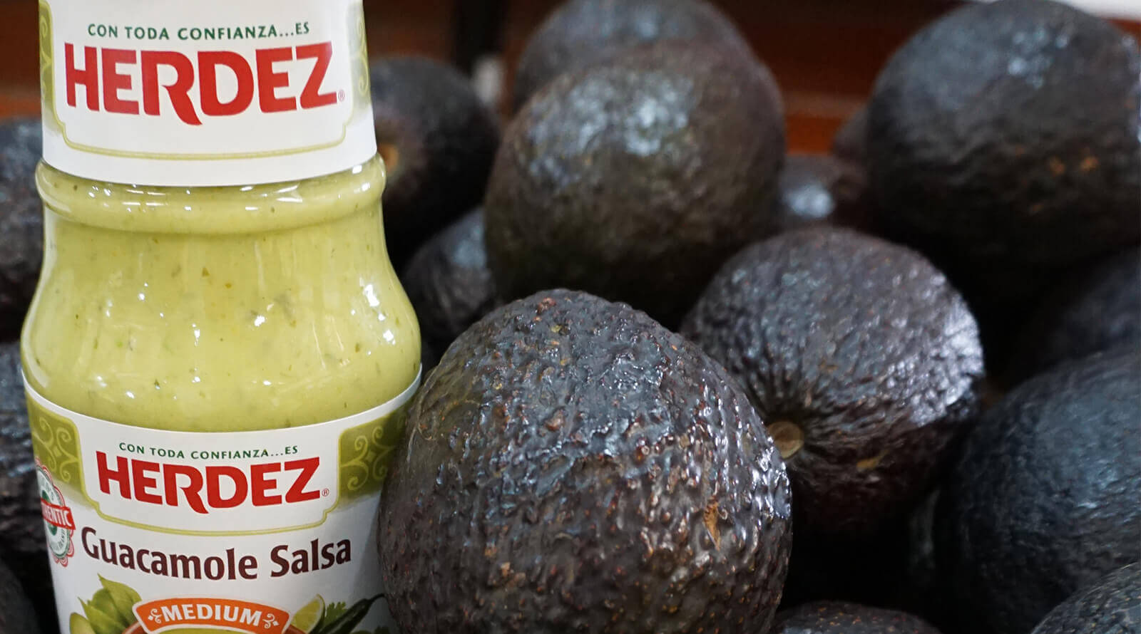 Herdez Guacamole Salsa jar surrounded by real avocados