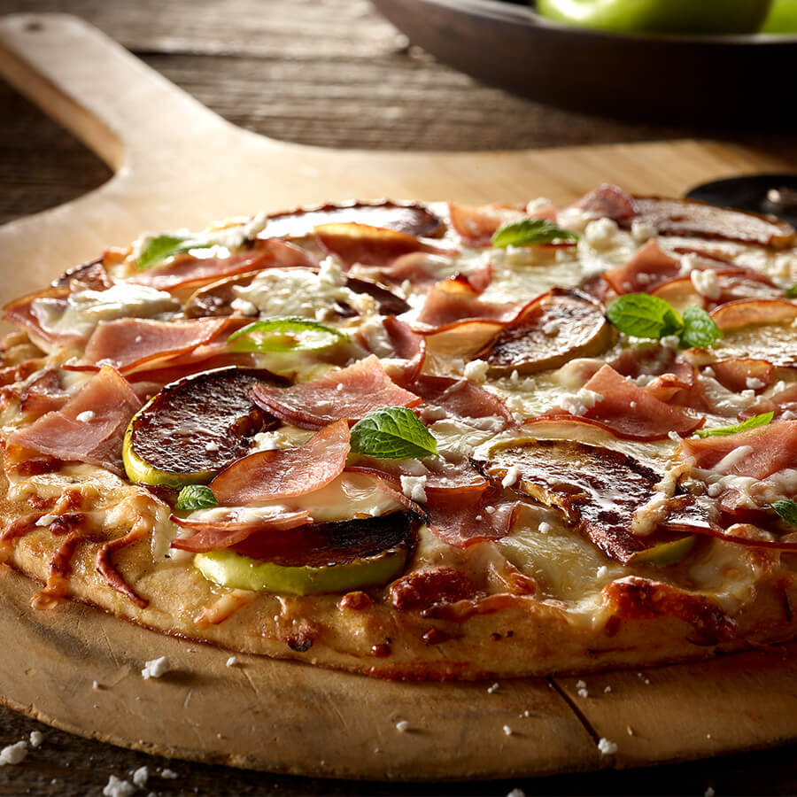 a pizza shot low to the survface, with apples, mint, and bacon