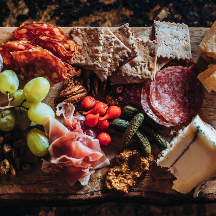 rustic charcuterie board with meats, fruit, cheeses & crackers shot from above in dramatic light