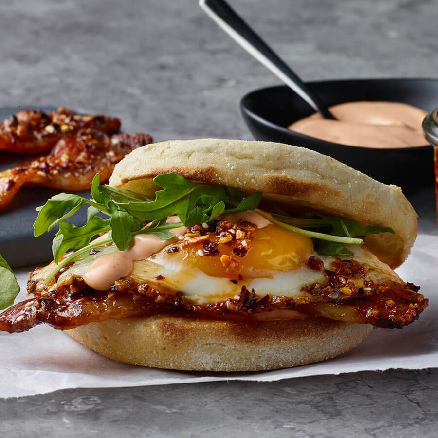egg sandwich with bacon, green garnish and chili crisp sauce