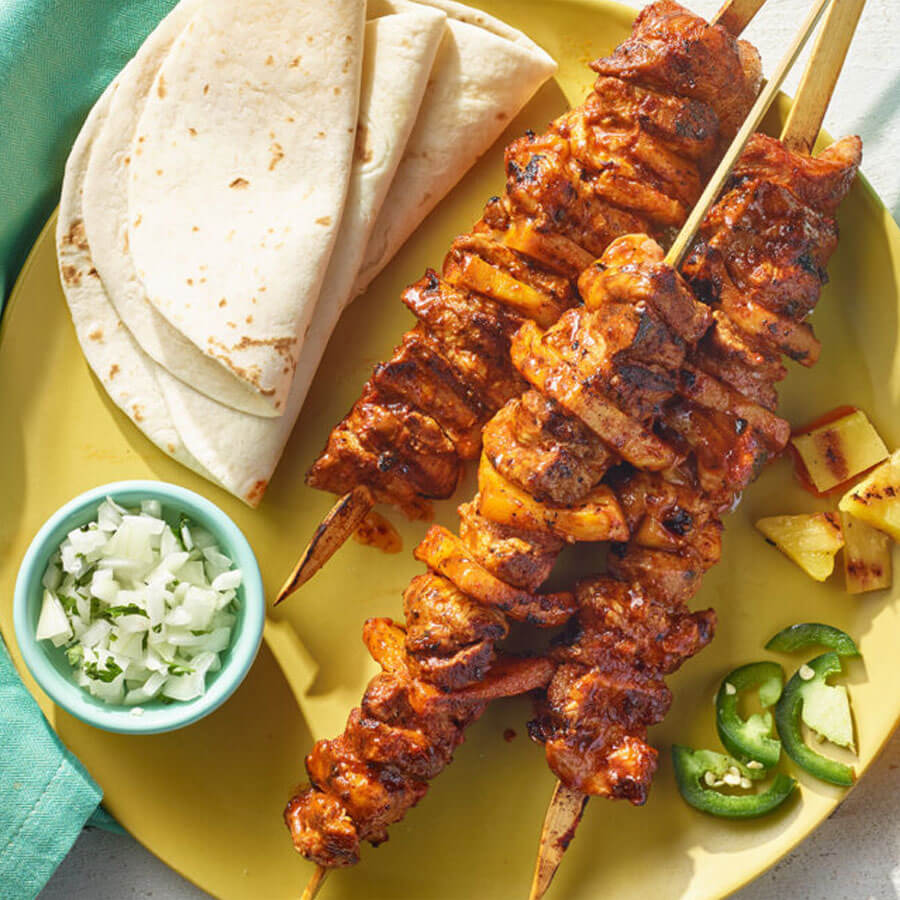 grilled chicken el pastor skewers on a yellow platter with pineapple & jalepeño slices