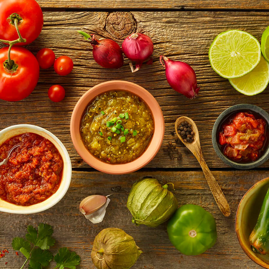 three small bowls with salsas in them, surrounded by whole ingredients
