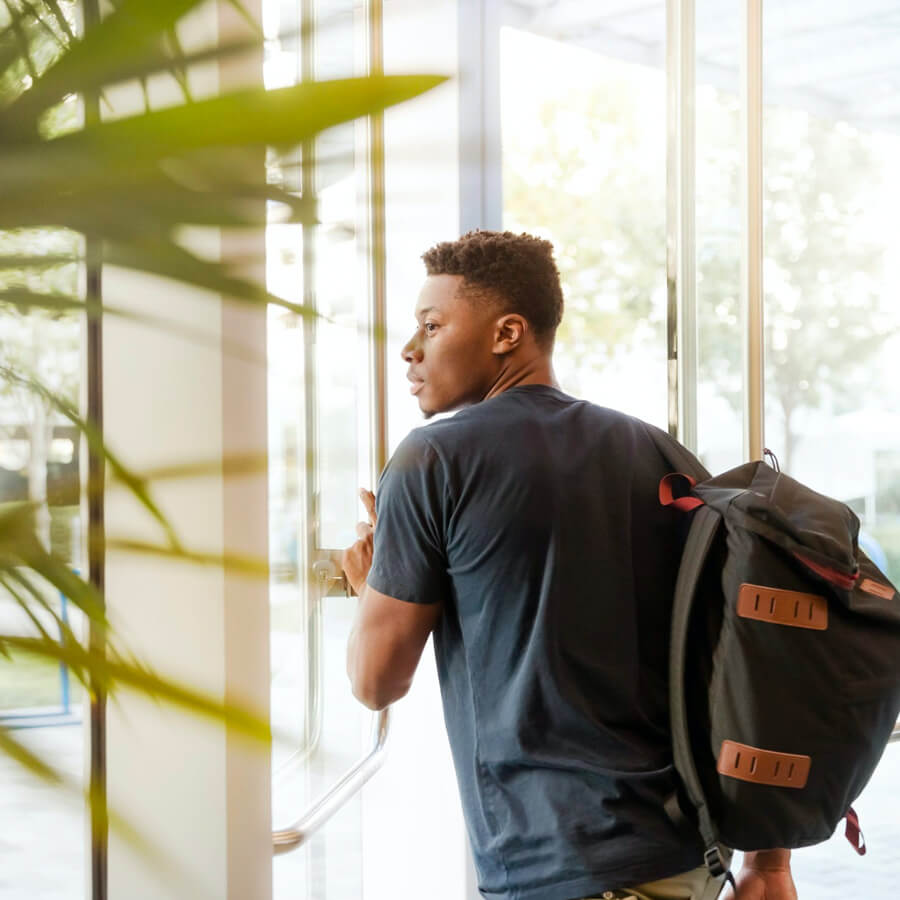 a male student with a backpack exiting a glass door