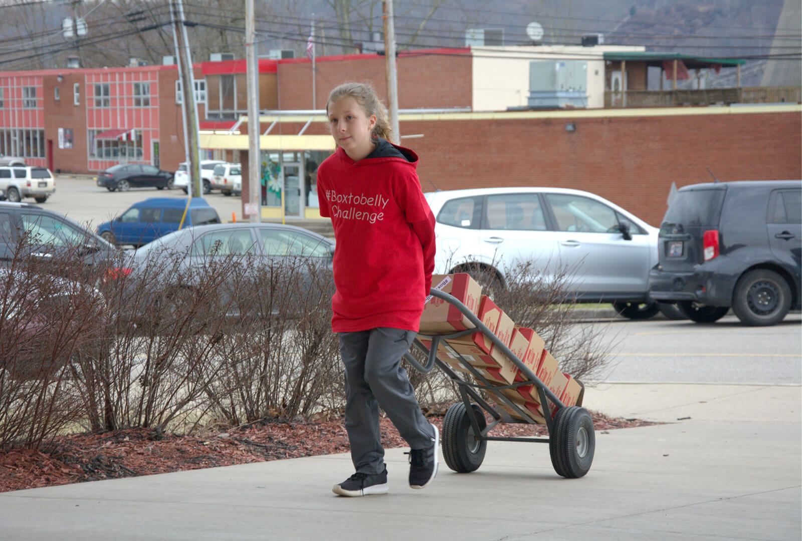 Elise carts a stack of donation boxes on a sidewalk