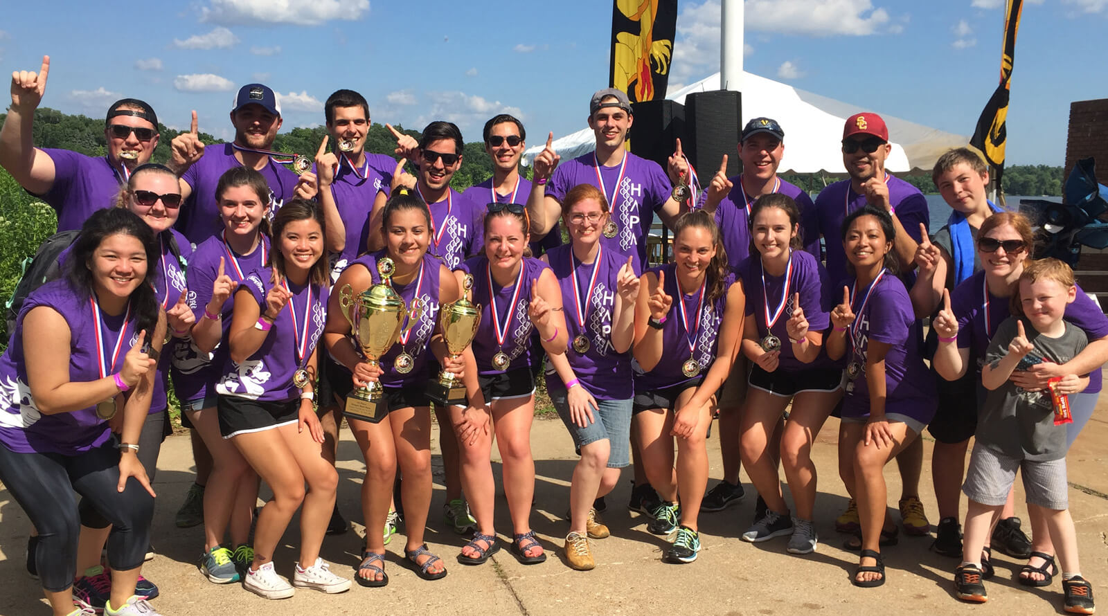 a large group of young people wearing purple shirts, all with index fingers extended indicating they are Number 1 and they have the trophies to prove it