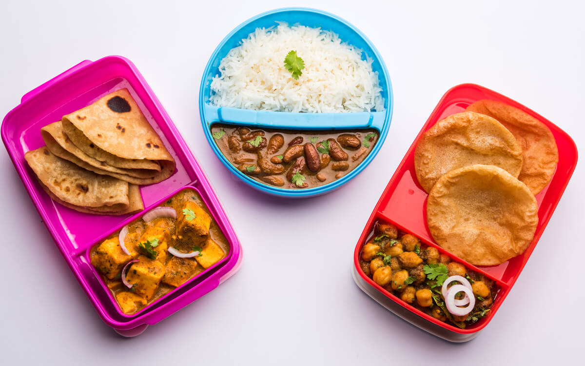 Three trays of Indian school lunch options on a table