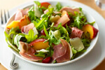 A plate of prosciutto, Arugula and pickled stone fruit salad