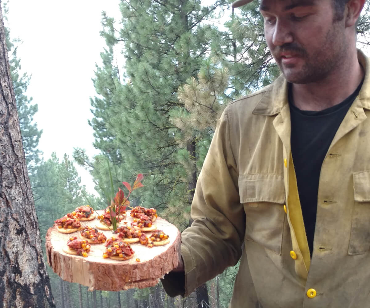 A firefighter holding a platter of some prepared SPAM in the woods